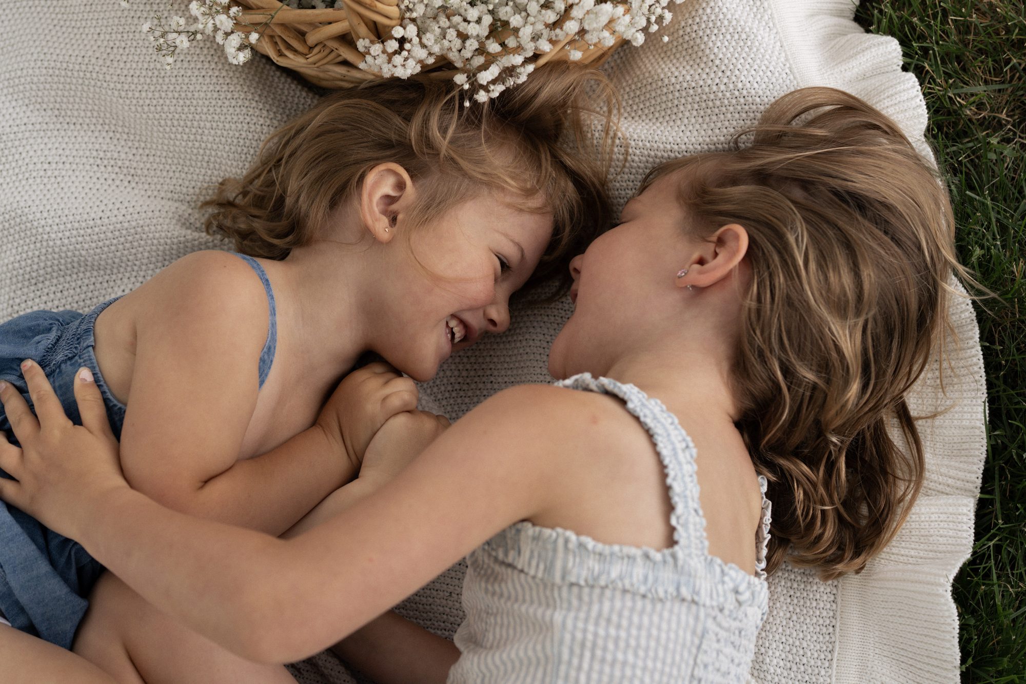 Two little girls snuggled nose to nose on a blanket, laughing