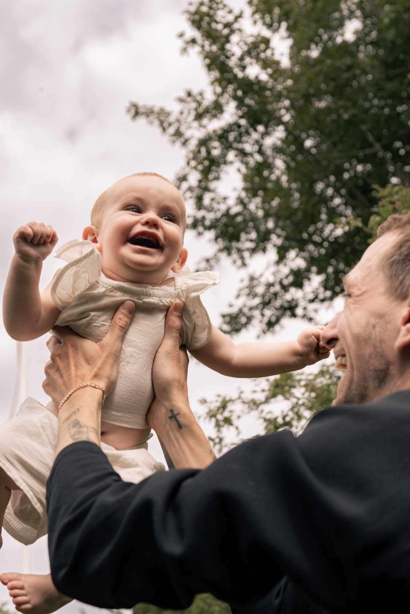 A laughing baby lifted into the air by her dad